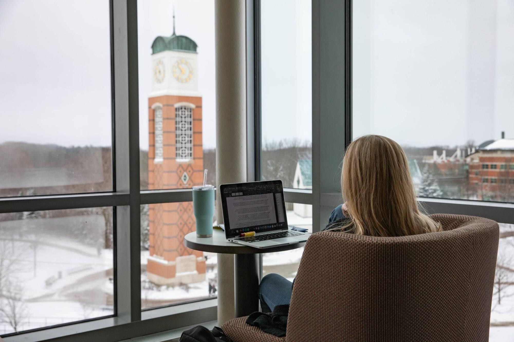 photo of student looking at computer with clock tower in the background